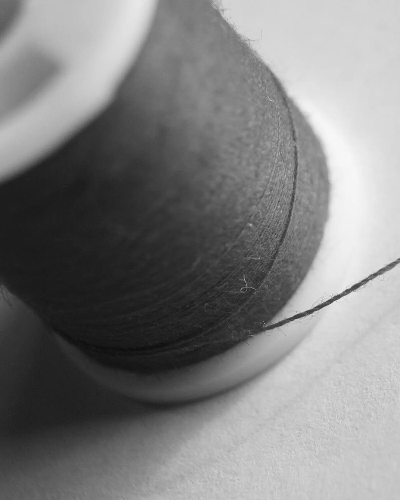 A single spool of thread with one strand drawn out across a pale ground.